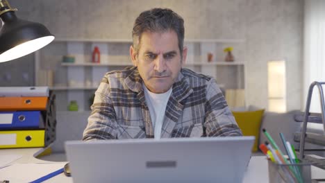 Mature-focused-man-working-in-home-office-using-laptop,-typing-on-keyboard.
